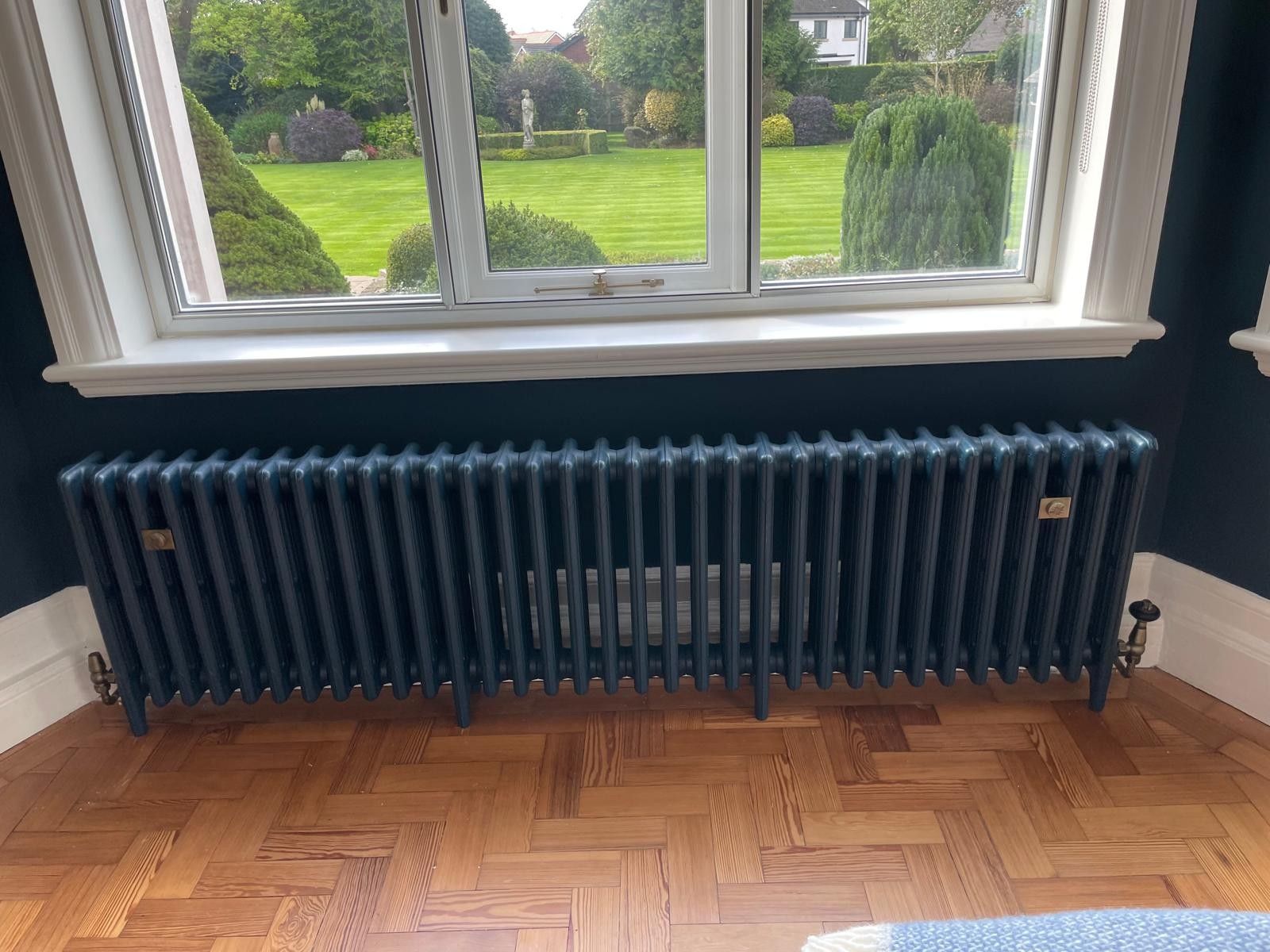 Dark blue cast iron column radiator installed beneath a sash window