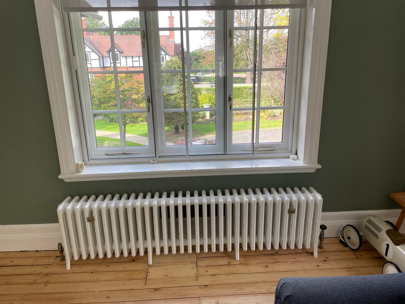 White cast iron radiator fitted against a sage green wall in a Manchester living room
