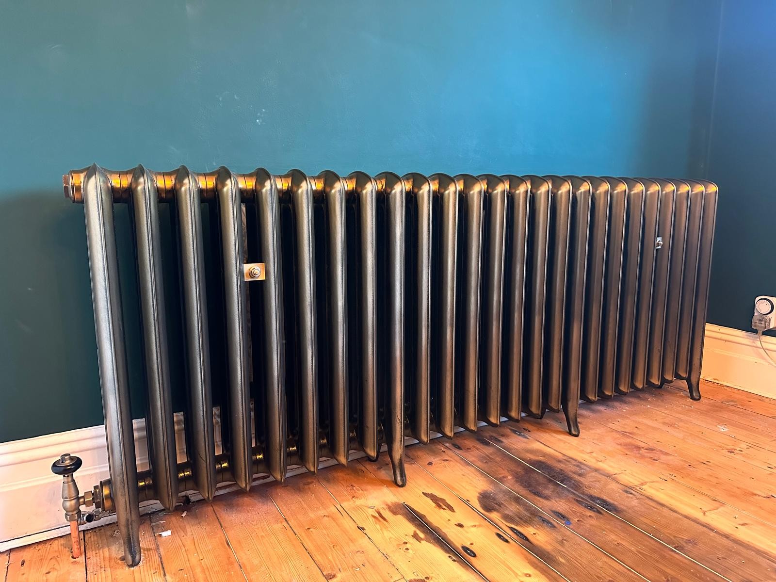 Long gunmetal cast iron radiator fitted against a teal wall in Trafford